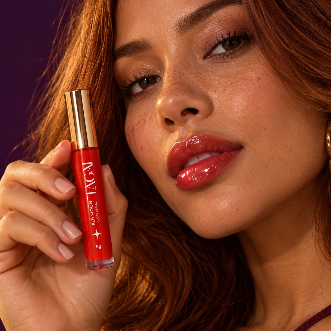 Mulher com os lábios brilhantes usando o Gloss Labial Red Moon 5g da Lagai, segurando o frasco vermelho com tampa dourada.