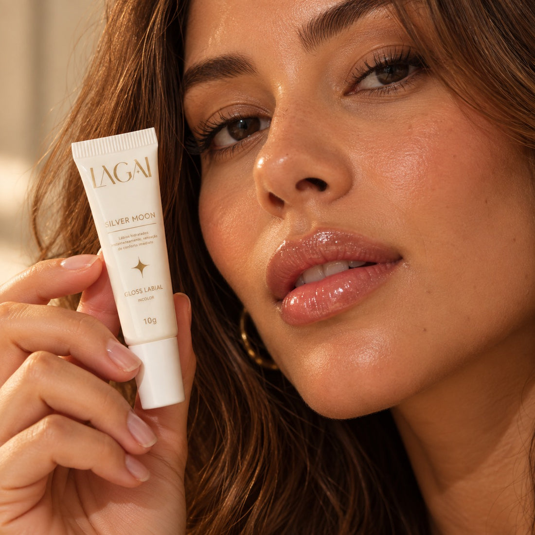 Mulher com os lábios brilhantes usando o Gloss Labial Silver Moon 10g incolor da Lagai, segurando a bisnaga branca.