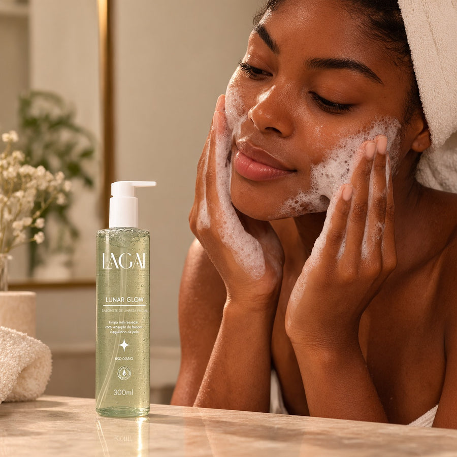 Mulher lavando o rosto com espuma do Sabonete Facial Lunar Glow 300ml da Lagai, frasco com gel verde na bancada do banheiro.
